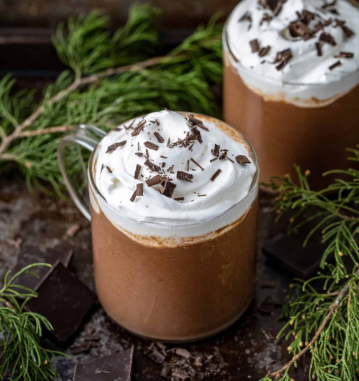 Glasses of Chocolate Eggnog on a table with evergreen and chocolate.