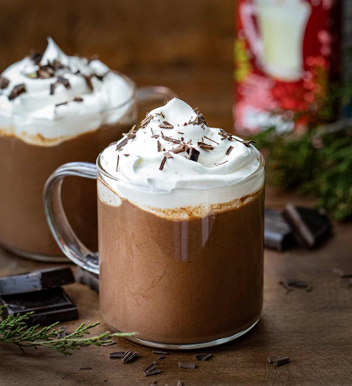 Glasses of Chocolate Eggnog with a container of eggnog in the background.