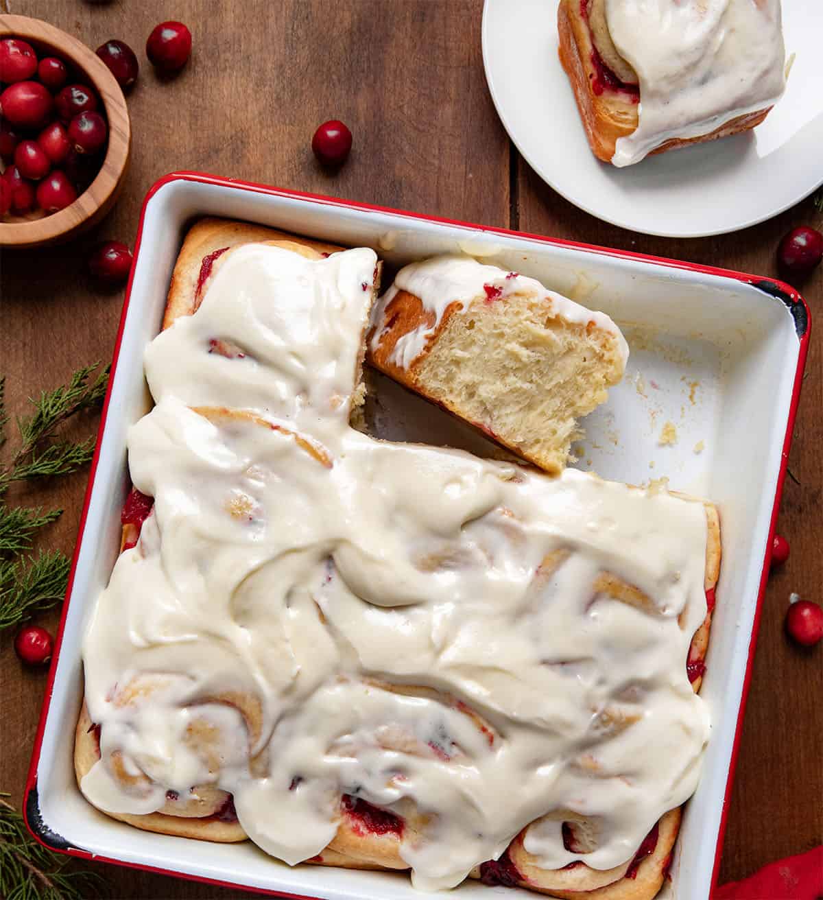 Pan of Cranberry Orange Sweet Rolls with one roll removed and one on its side on a wooden table from overhead.