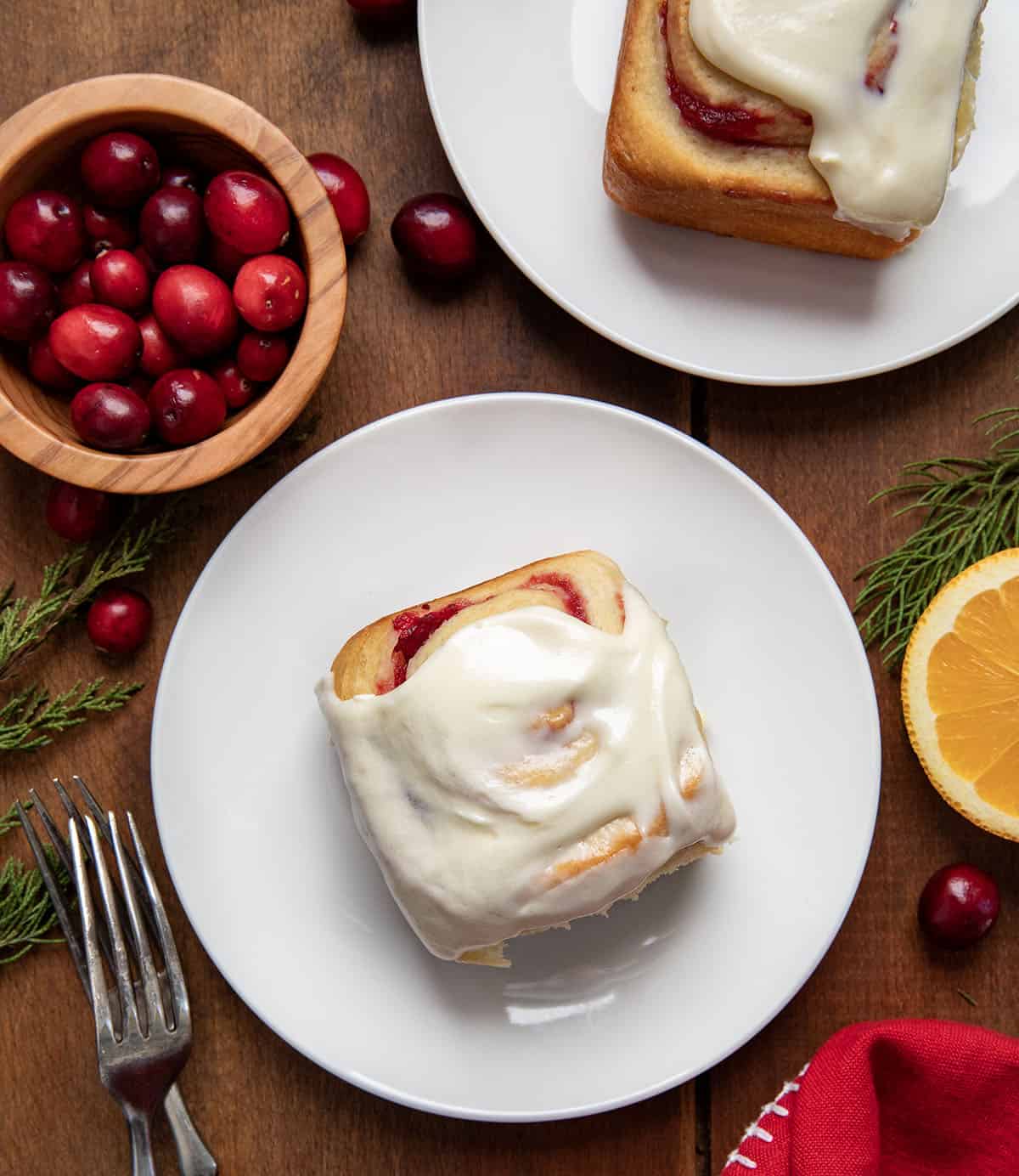 Cranberry Orange Sweet Rolls on white plates on a wooden table from overhead.