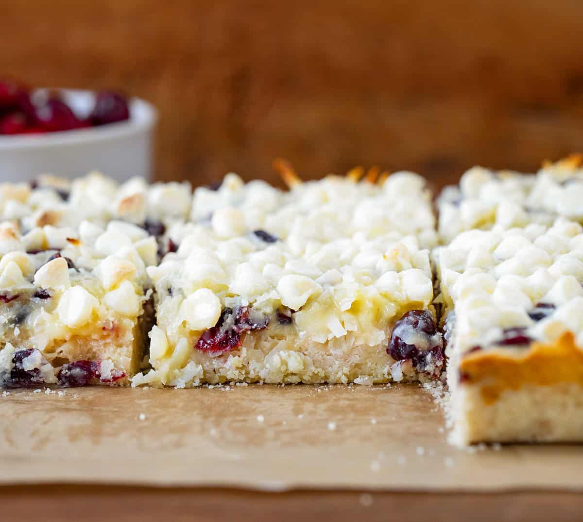 Cut up Cranberry White Chocolate Magic Bars on a piece of parchment paper on a wooden table.