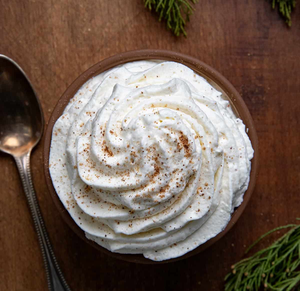 Looking down on a cup of Eggnog Whipped Cream on a wooden table.