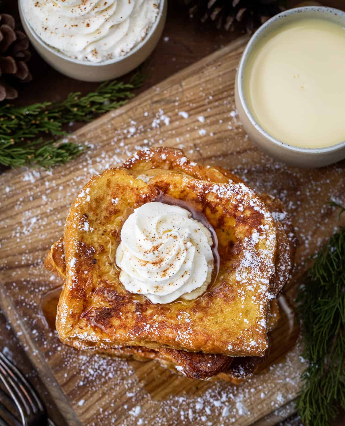 Looking down on a stack of Eggnog French Toast on a cutting board with a cup of egg nog and hot cocoa.