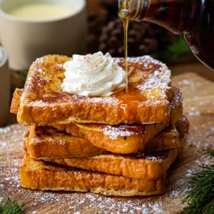 Pouring syrup over a stack of Eggnog French Toast on a cutting table.