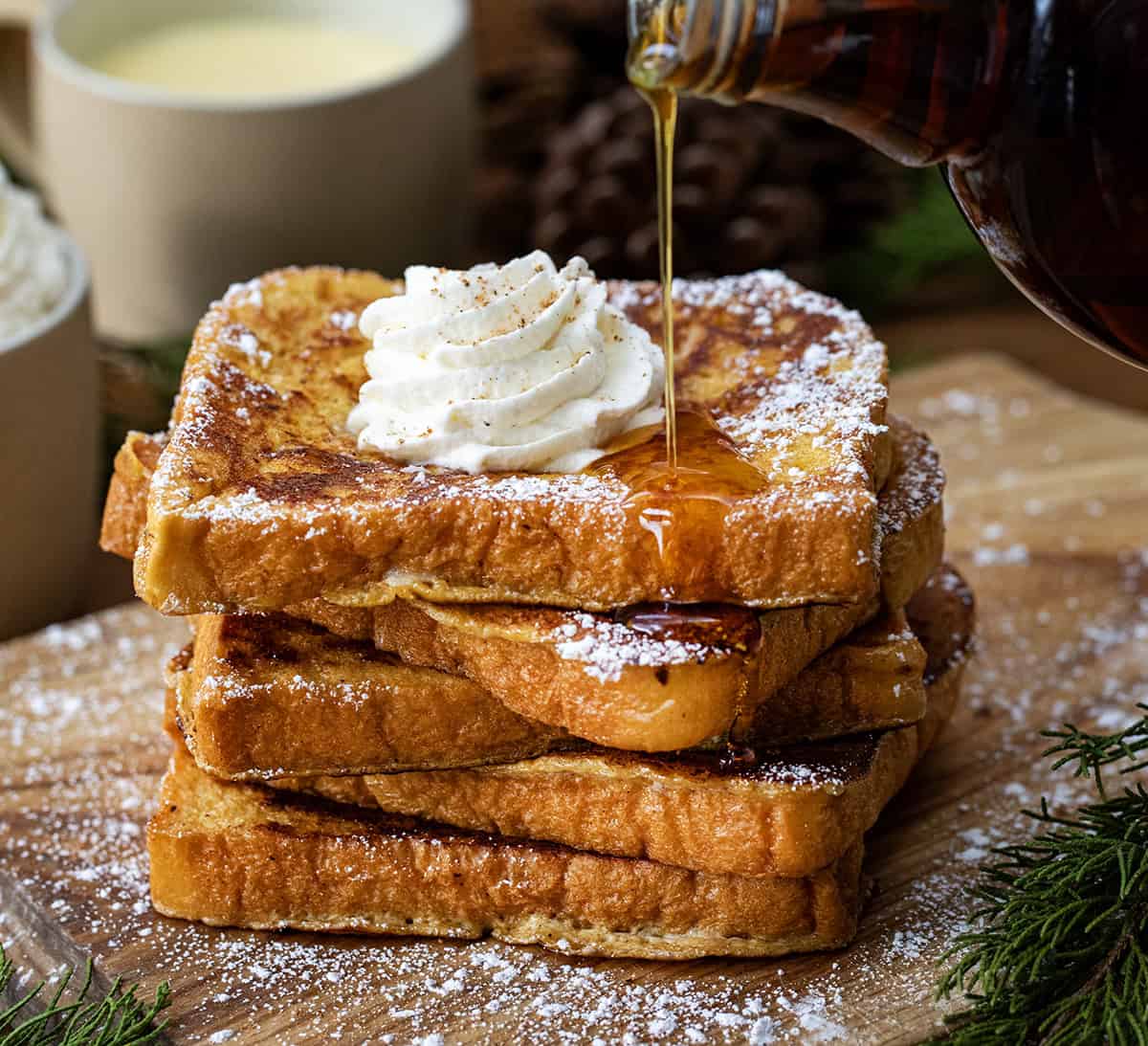 Pouring syrup over a stack of Eggnog French Toast on a cutting table. 