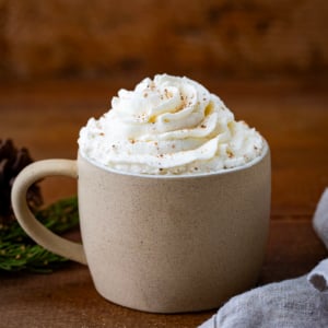 Mug of hot cocoa with Eggnog Whipped Cream topping on a wooden table.