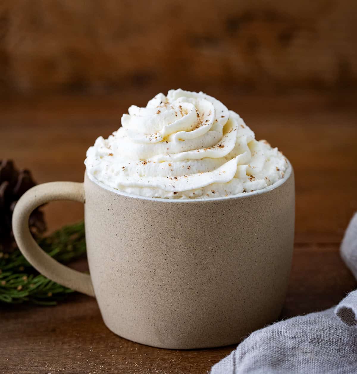 Mug of hot cocoa with Eggnog Whipped Cream topping on a wooden table. 