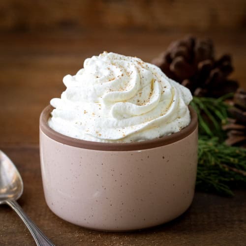 Cup of Eggnog Whipped Cream on a wooden table with a spoon.