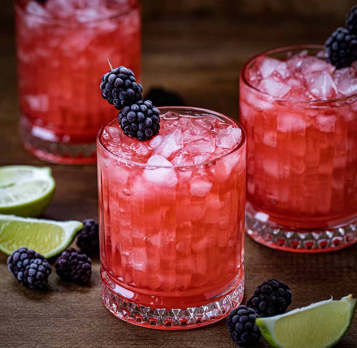 Glasses of Frosted Blackberry Bourbon Smash on a wooden table with limes and fresh blackberries.