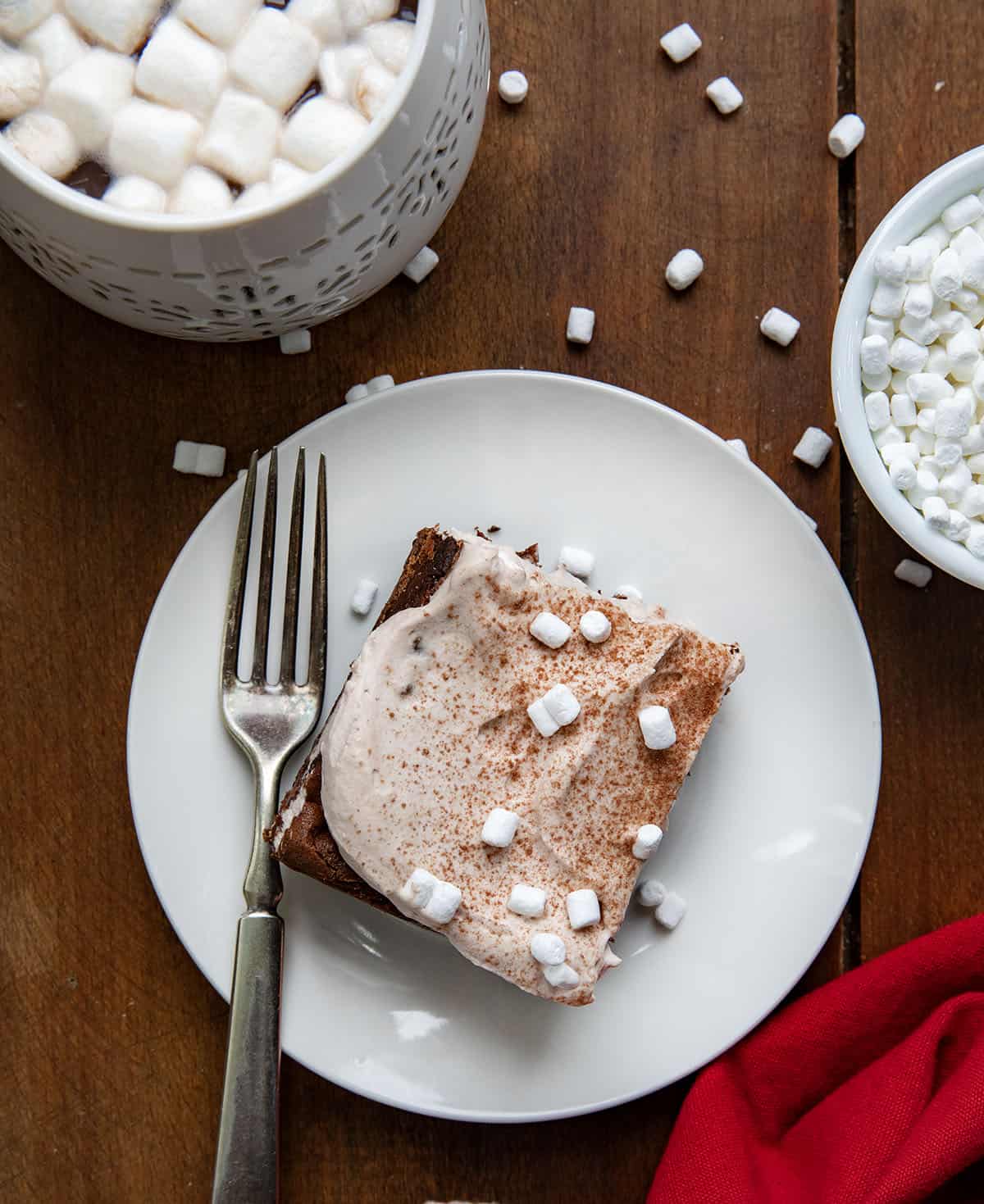 One Hot Chocolate Cheesecake Bar on a white plate with a fork on a wooden table from overhead.