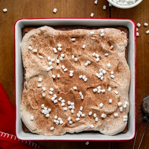 Hot Chocolate Cheesecake Bars in a white and red pan on a wooden table from overhead.