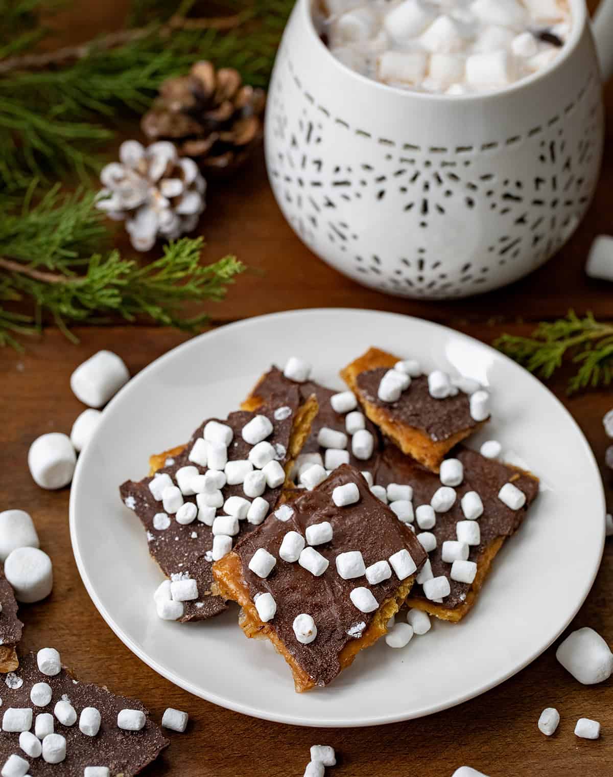 Plate of pieces of Hot Cocoa Christmas Crack with hot cocoa in the background on a wooden table.