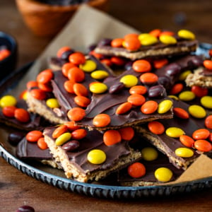 Reese's Pieces Peanut Butter Bark stacked on a tray on a wooden table.