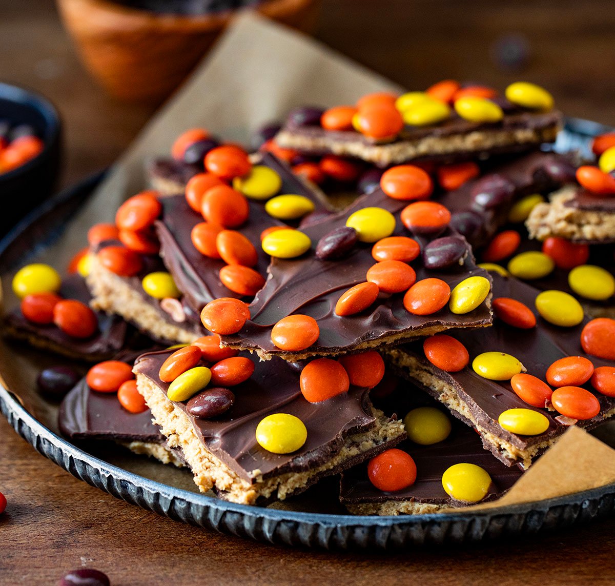 Reese's Pieces Peanut Butter Bark stacked on a tray on a wooden table.