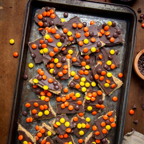 Reese's Pieces Peanut Butter Bark on a cookie sheet on a wooden table from overhead.