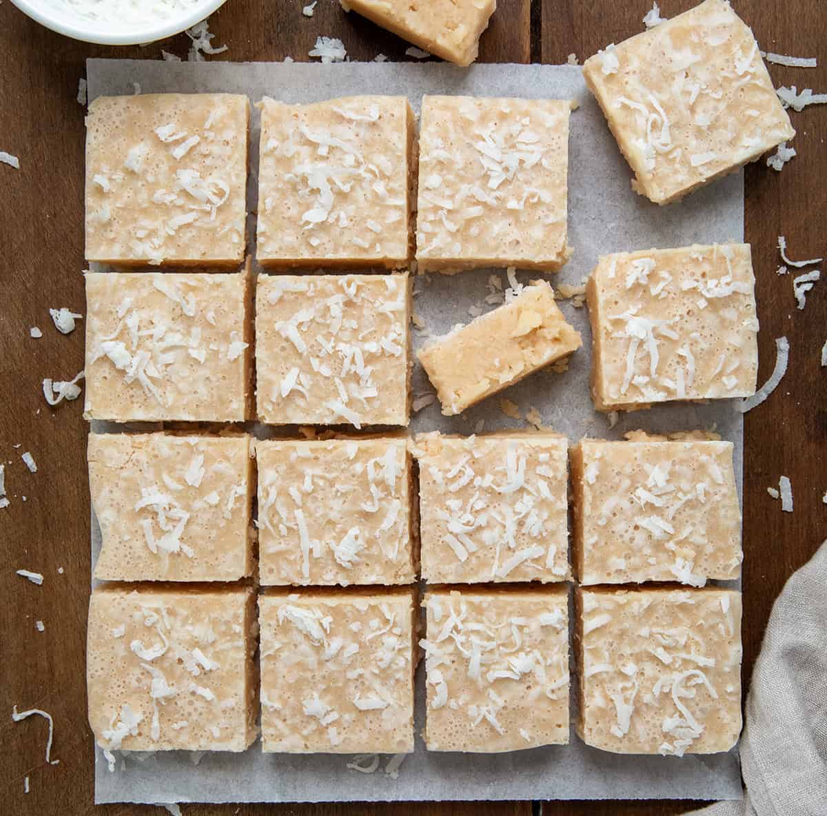 White Coconut Fudge cut into pieces on a piece of parchment on a wooden table from overhead. 