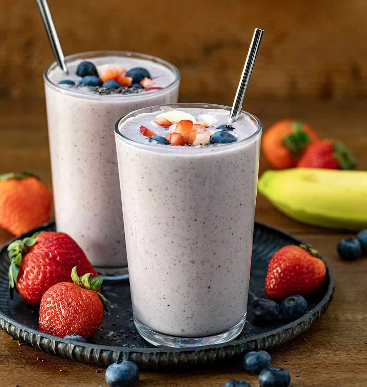 Two glasses of High Protein Berry Bliss Smoothie on a tray on a wooden table. 