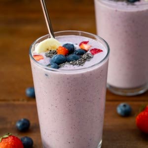 Glasses of High Protein Berry Bliss Smoothie on a wooden table with fresh fruit around.