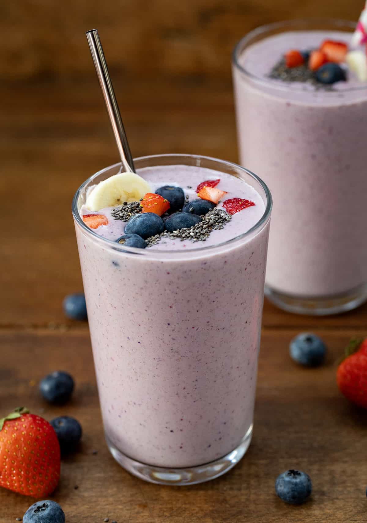 Glasses of High Protein Berry Bliss Smoothie on a wooden table with fresh fruit around.