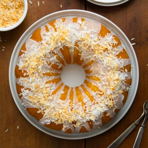 Whole Coconut Pound Cake on a white platter on a wooden table from overhead.