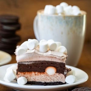 One Hot Chocolate Lasagna Bar on a white plate with hot cocoa and oreos in the background.