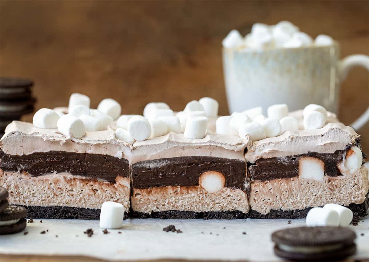 Hot Chocolate Lasagna Bars on a piece of parchment paper with oreos and hot cocoa in the background.