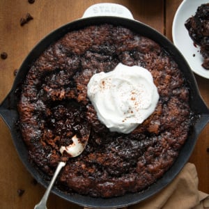 Skillet of Hot Fudge Pudding Cake with whipped cream and a spoon in the pan.