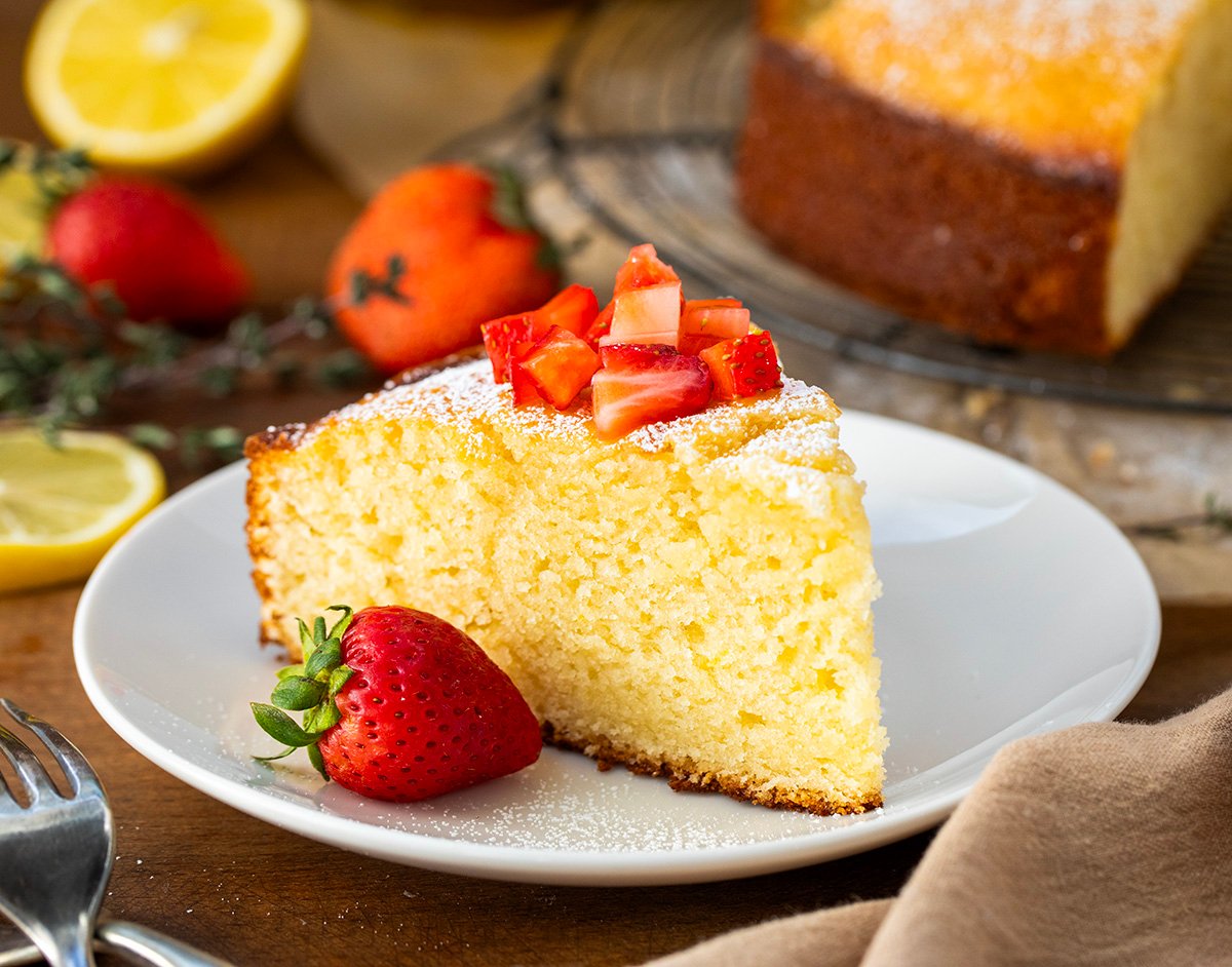 Piece of Olive Oil Cake on a plate with fresh strawberries and lemon.