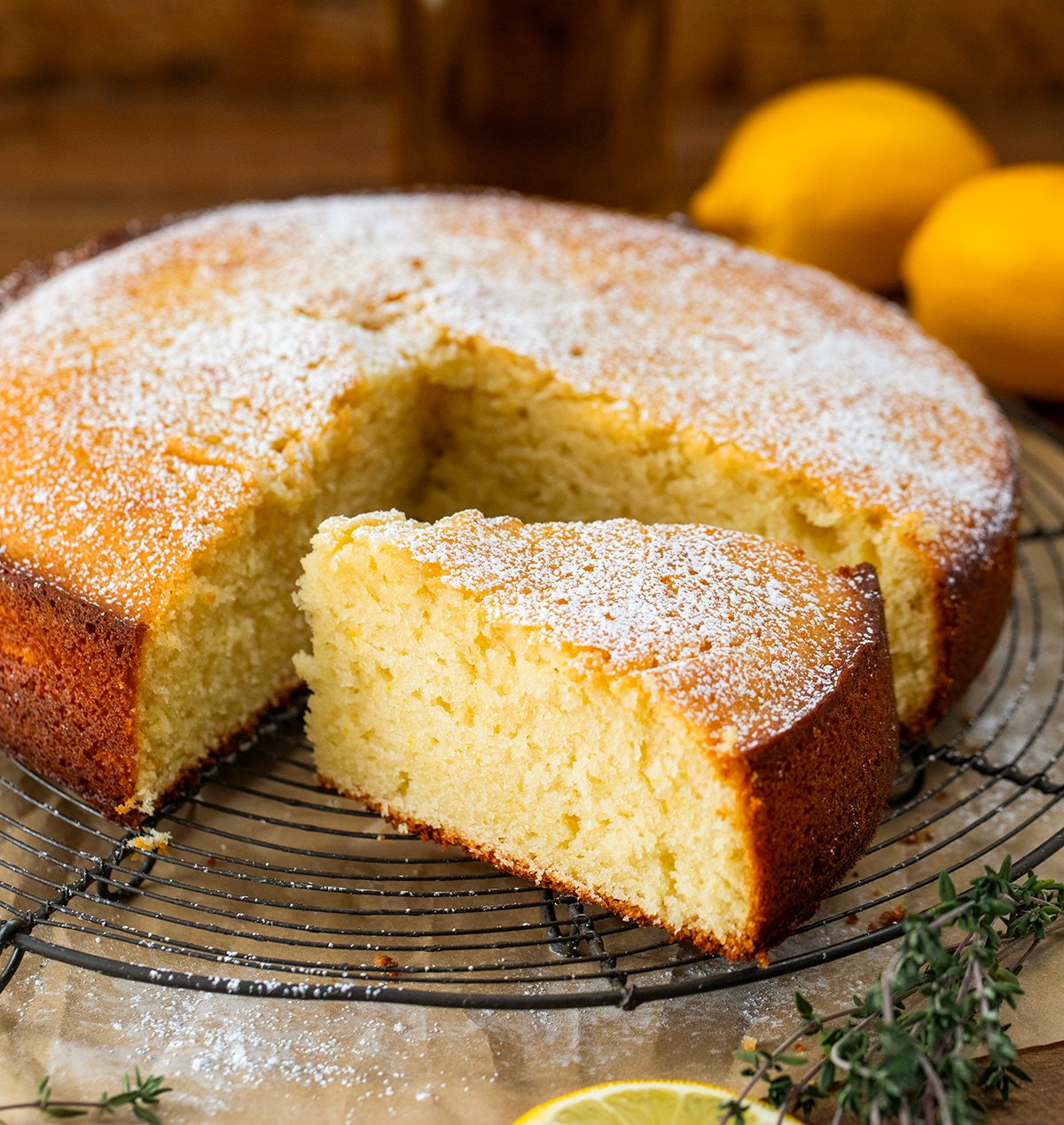 Olive Oil Cake on a rack on a wooden table with a piece cut.