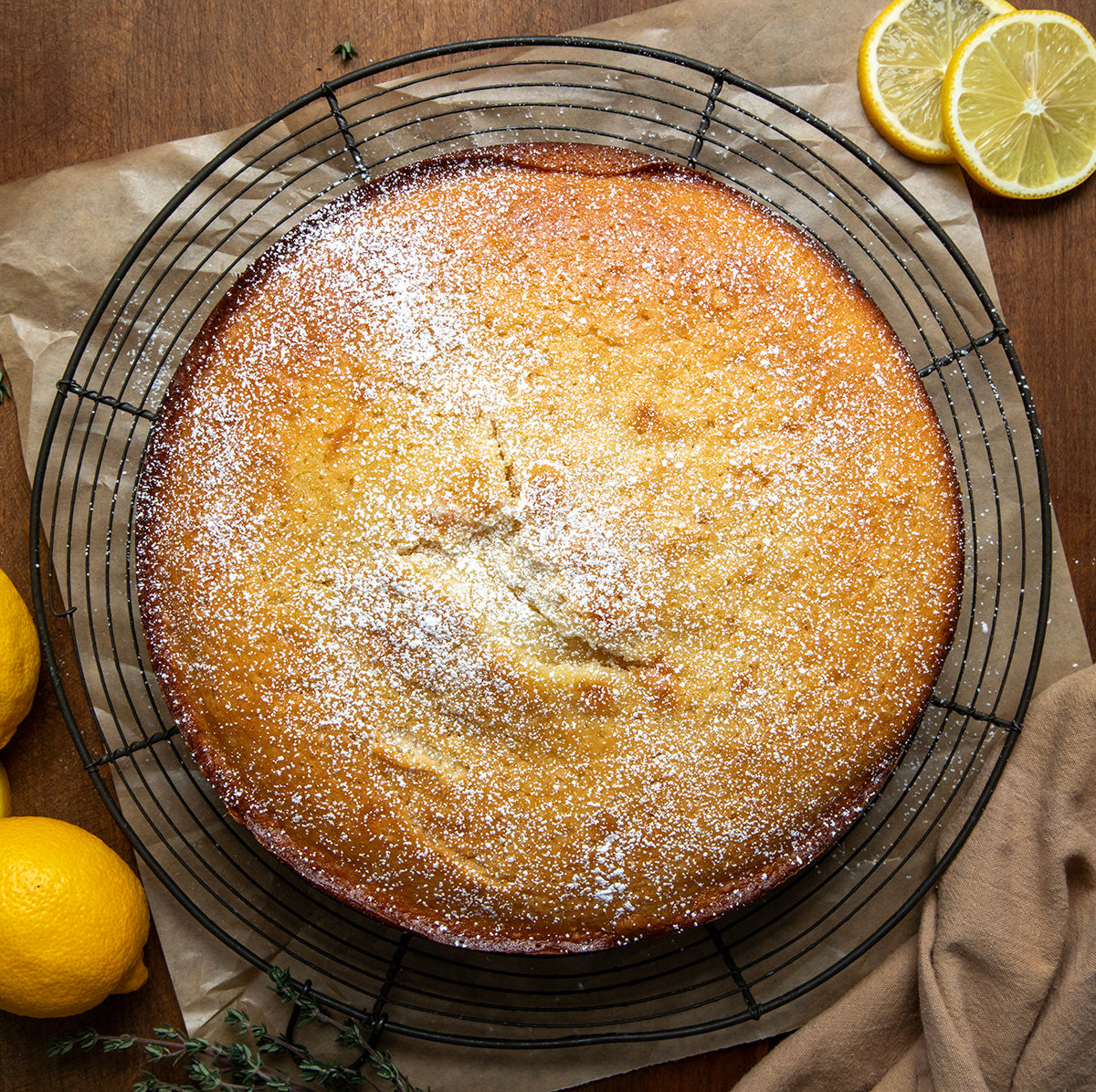 Olive Oil Cake on a rack on a wooden table from overhead with fresh lemon.