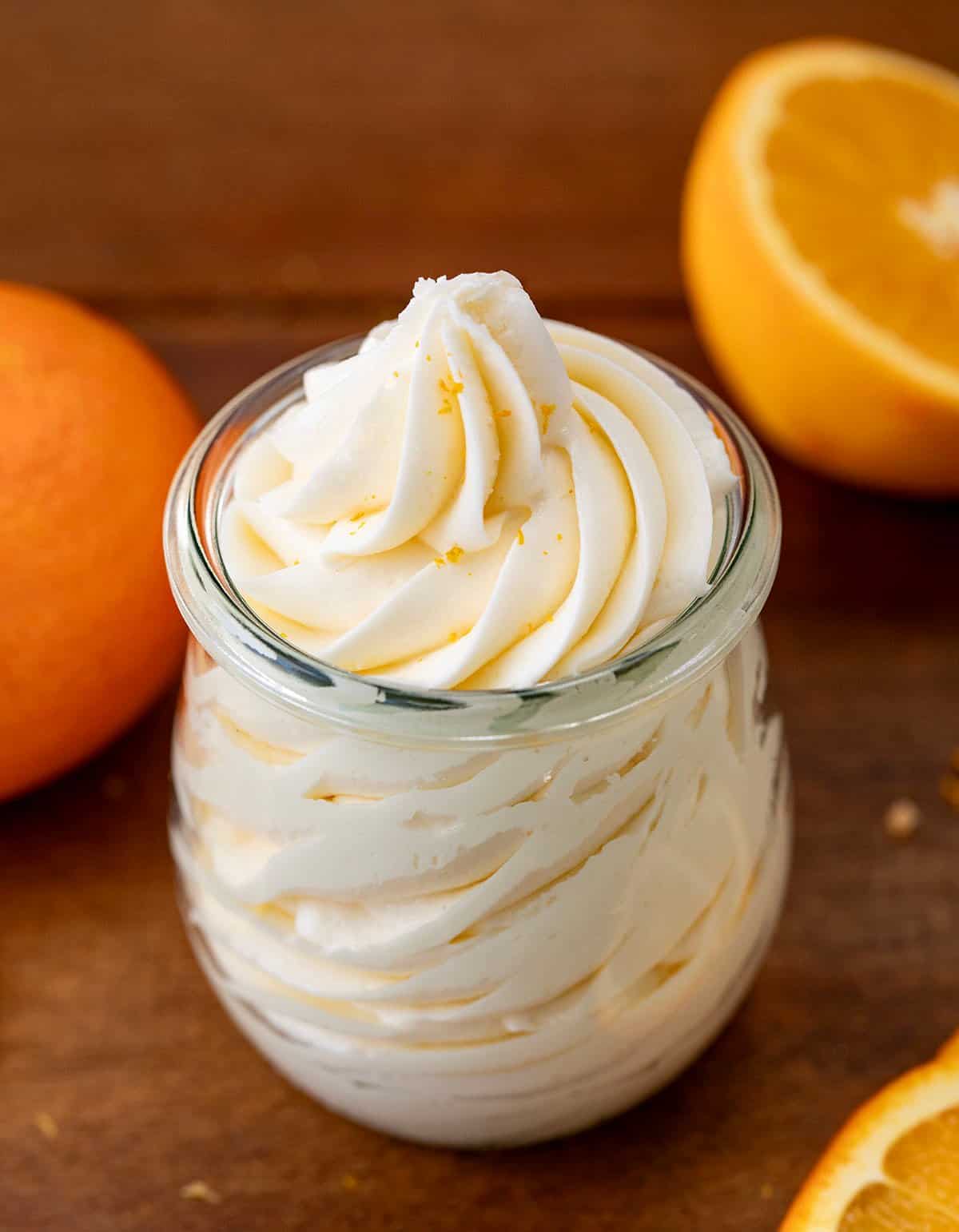 Jar of piped Orange Creamsicle Buttercream on a wooden table with fresh orange slices.