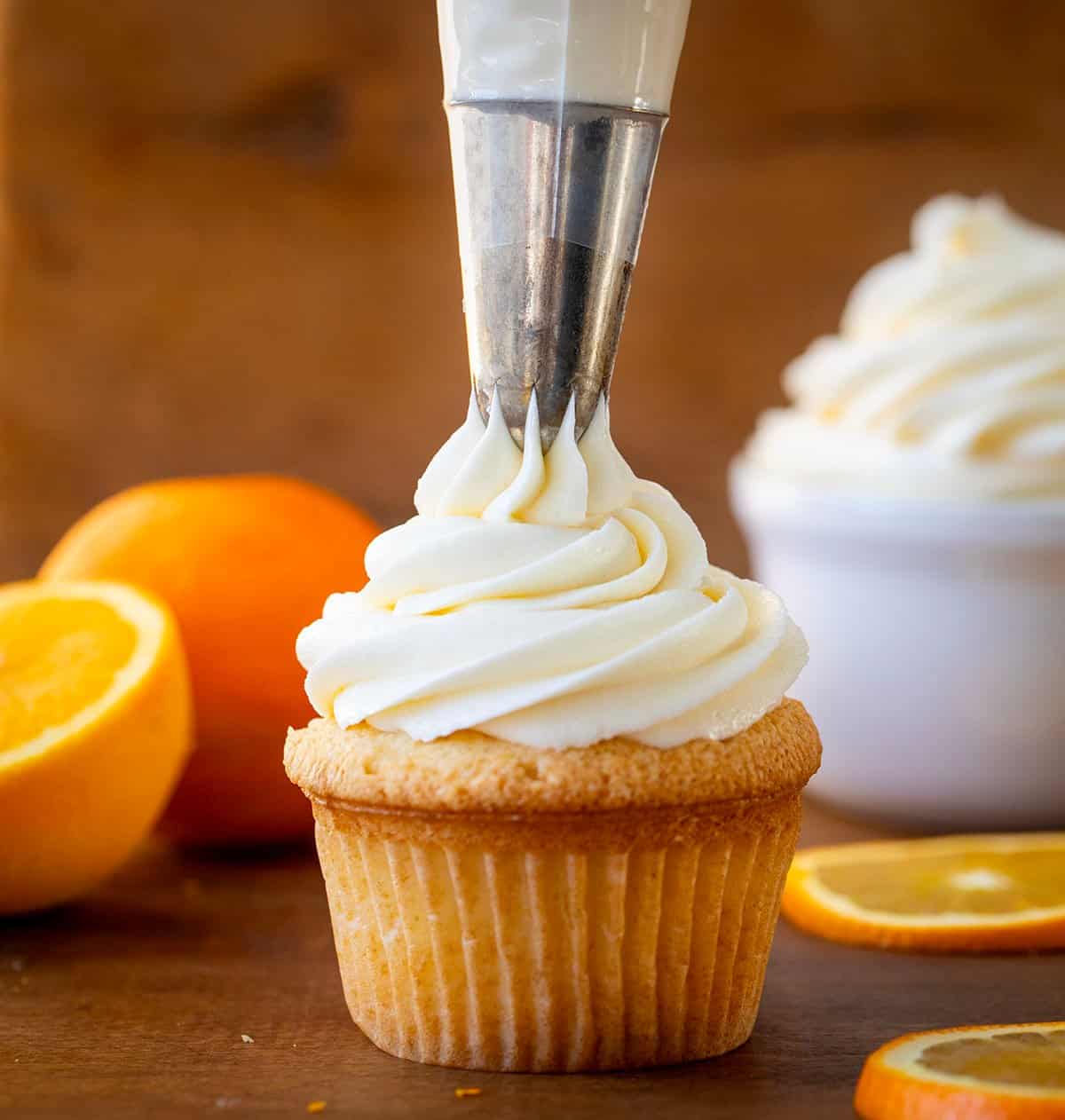 Piping Orange Creamsicle Buttercream onto a cupcake with orange slices around.