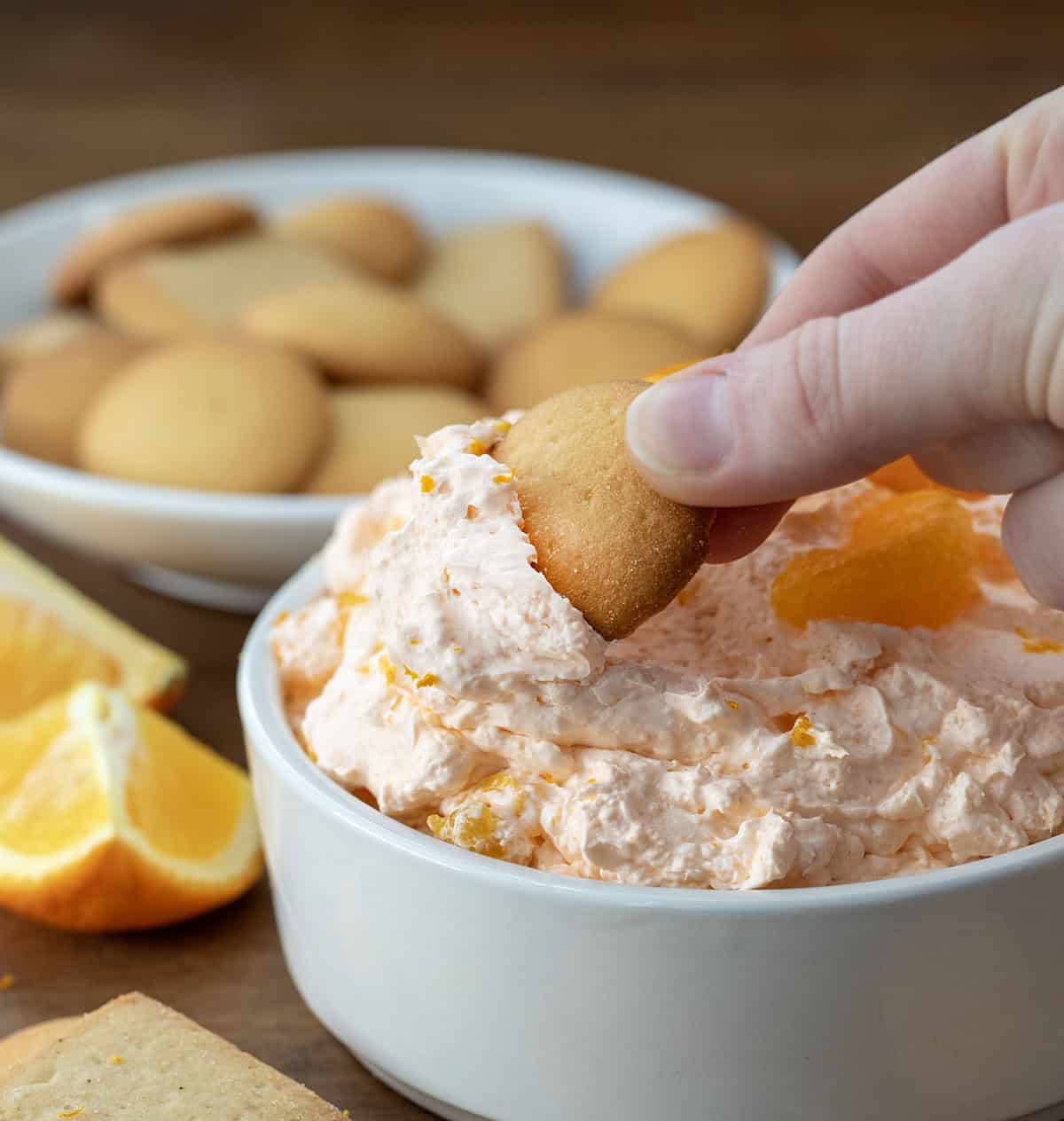 Hand dipping a vanilla wafer into Orange Creamsicle Dream Dip.