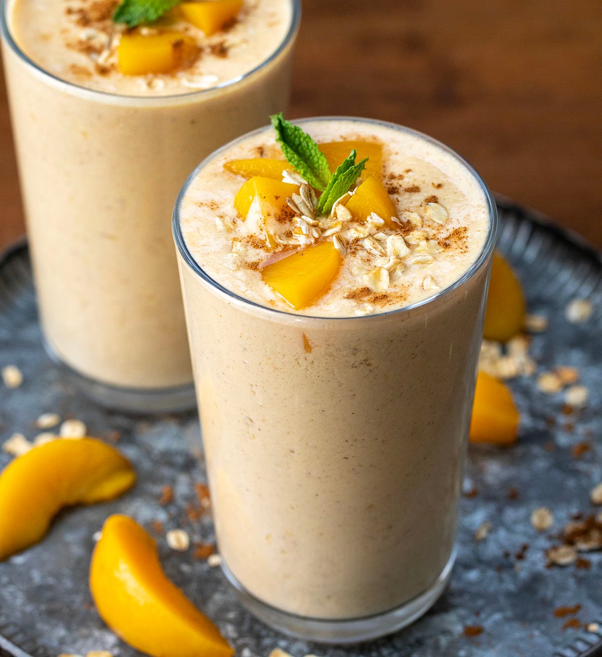 Peach Cobbler Smoothies on a tray with fresh peaches.