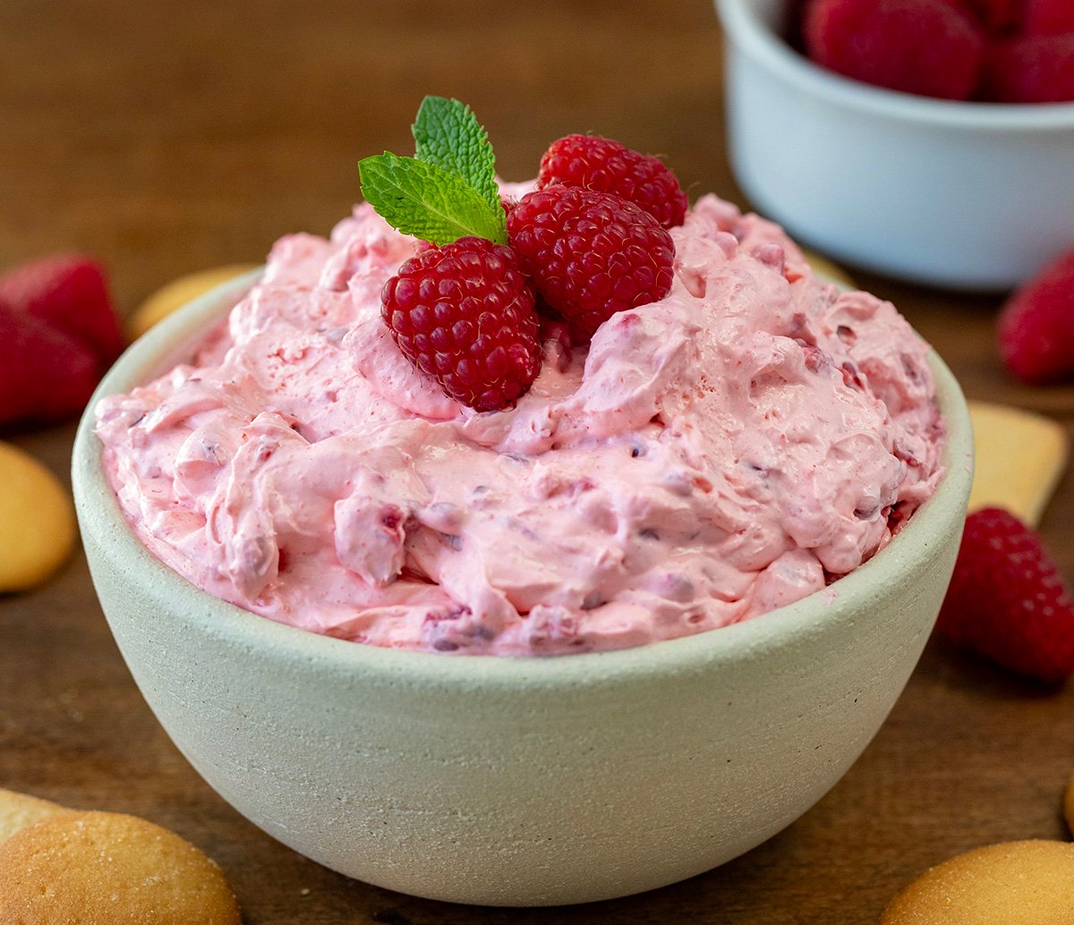 Bowl of Raspberry Cheesecake Dip on a wooden table with vanilla wafers.