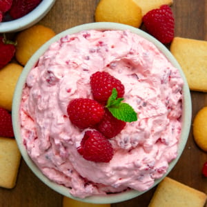 Bowl of Raspberry Cheesecake Dip on a wooden table with vanilla wafers from overhead.