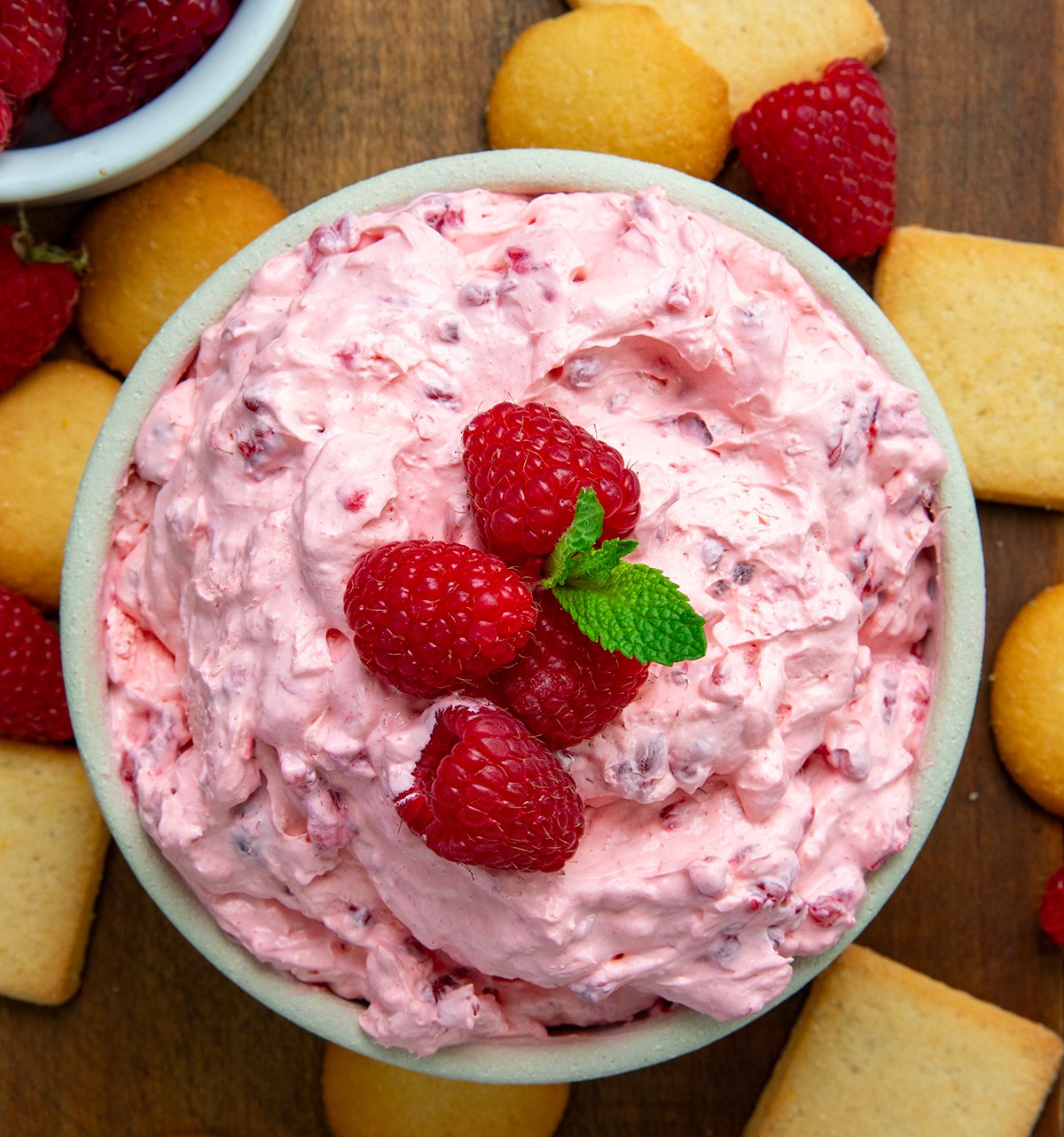 Bowl of Raspberry Cheesecake Dip on a wooden table with vanilla wafers from overhead.