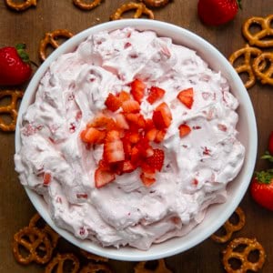 Bowl of Strawberry Dream Dip on a wooden table surrounded by pretzels and fresh strawberries.