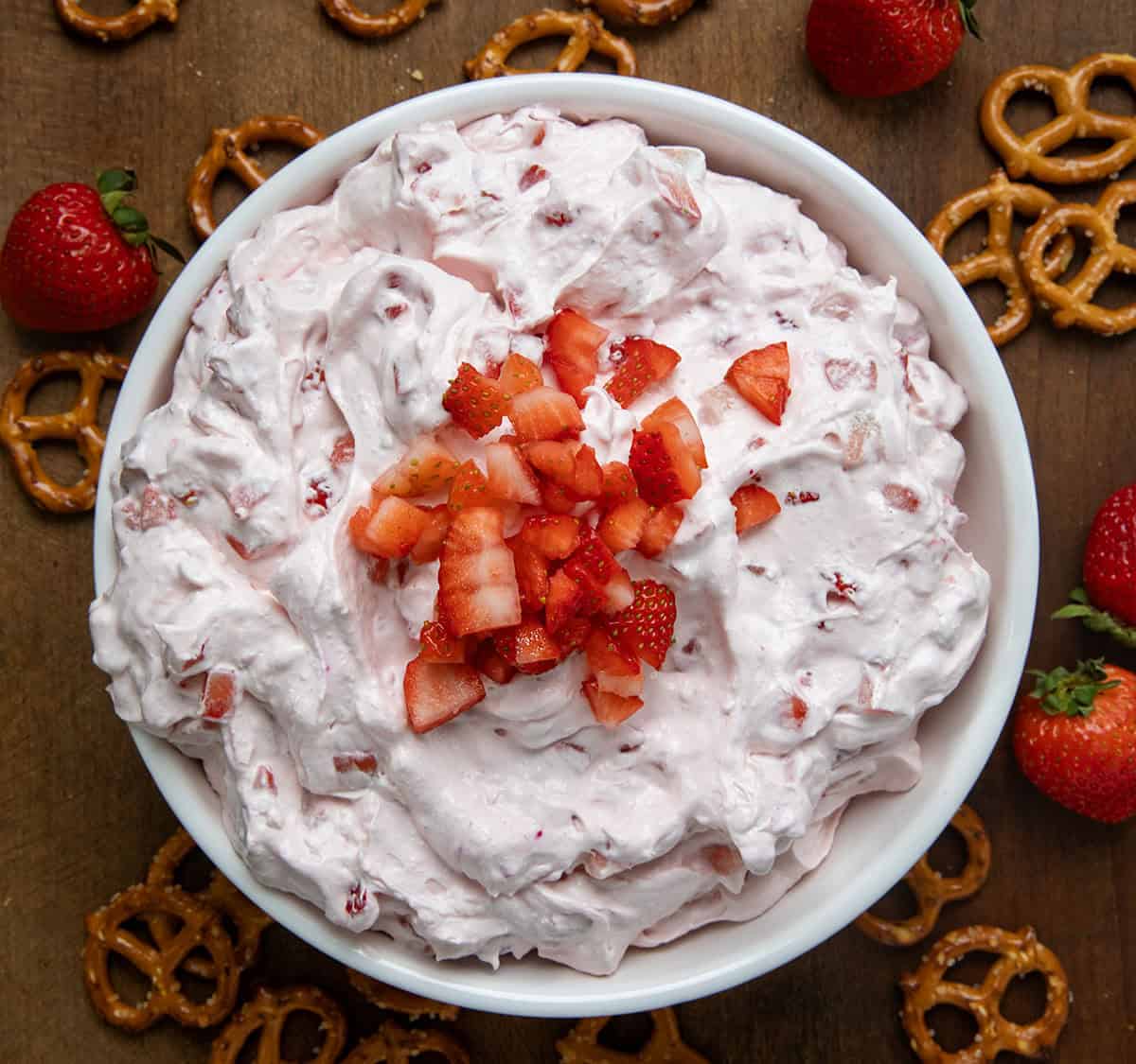 Bowl of Strawberry Dream Dip on a wooden table surrounded by pretzels and fresh strawberries. 