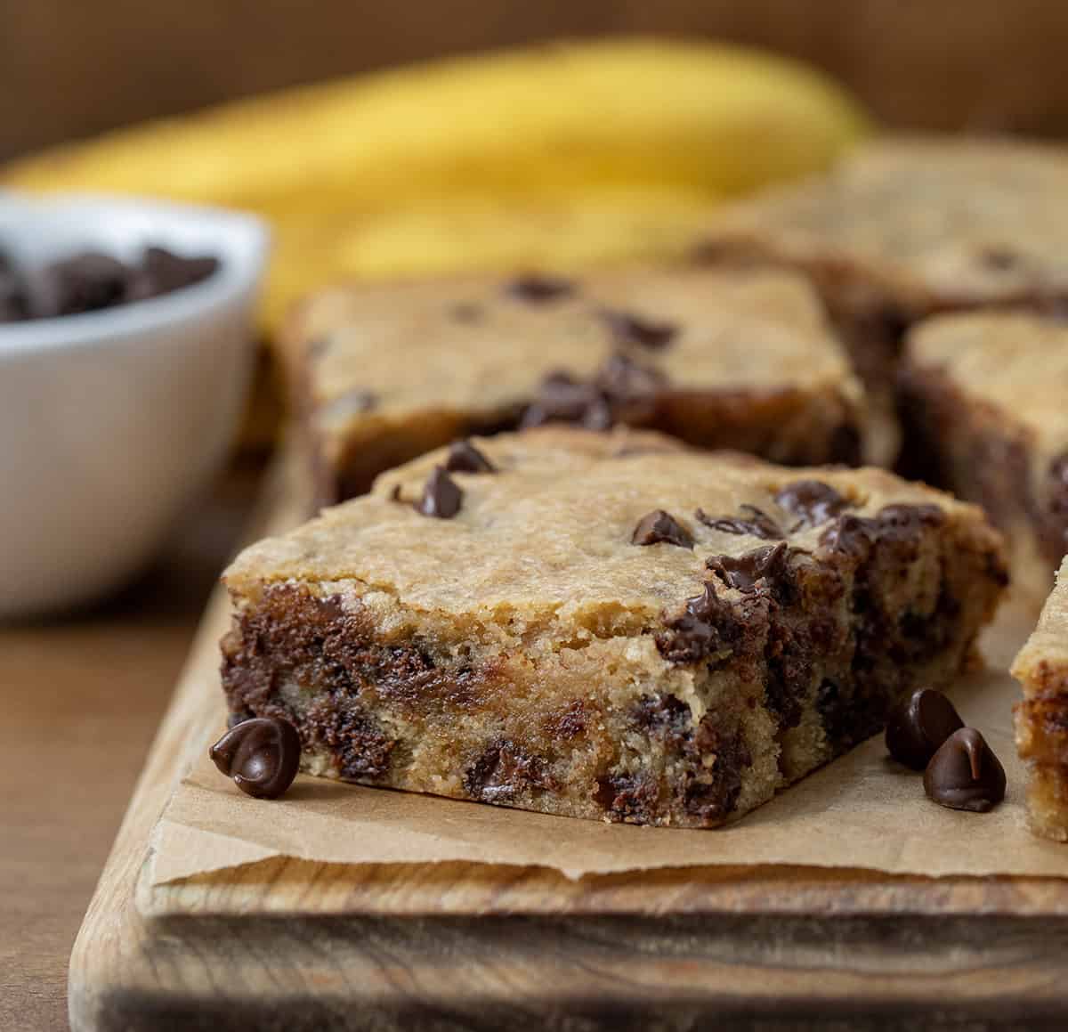 Banana Chocolate Chip Bars on a cutting board with bananas in the background.