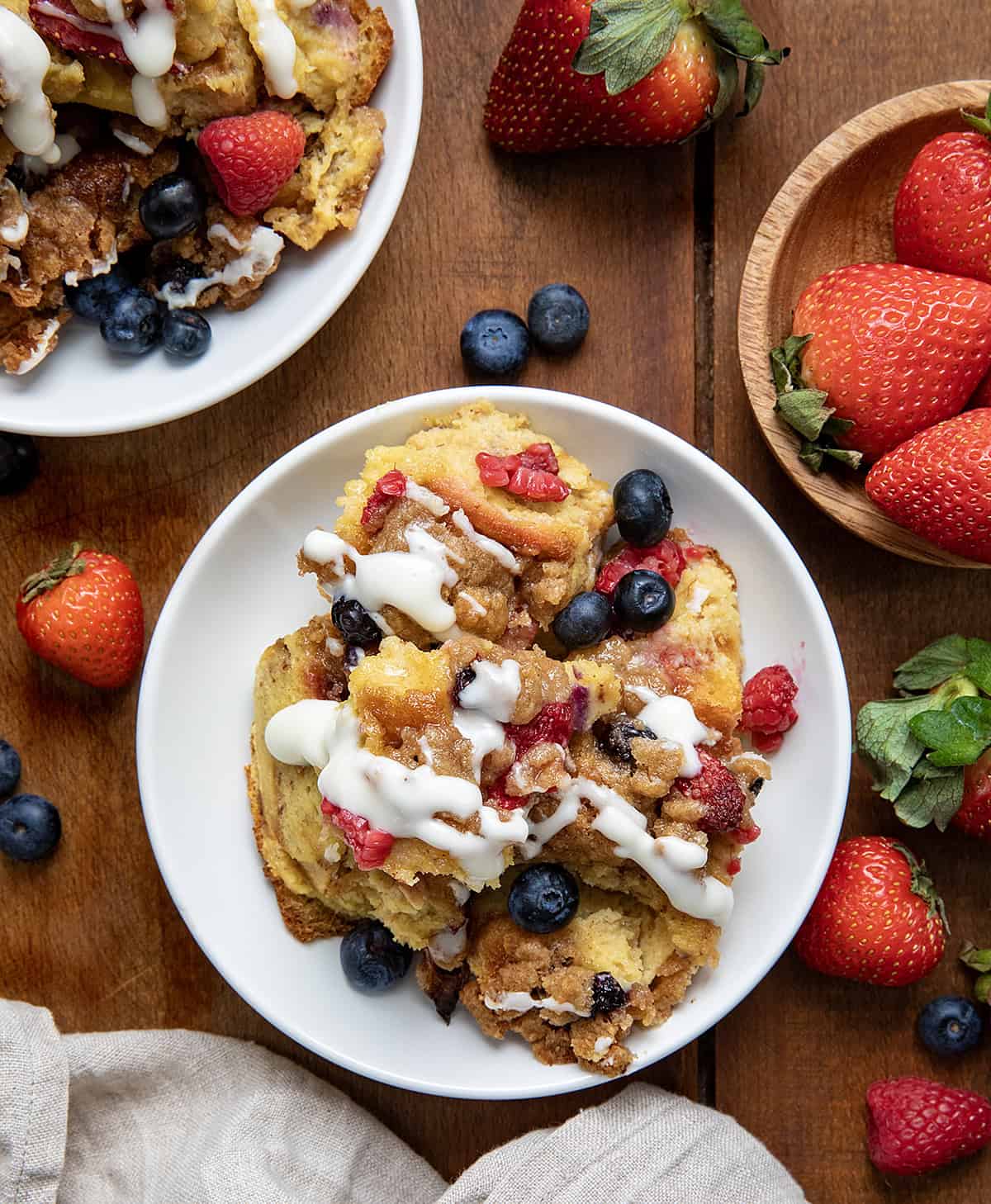 Plates of Berries and Cream Overnight French Toast Bake on a wooden table with fresh fruit all around.