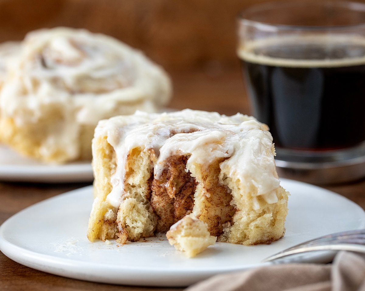 Bit into Biscuit Cinnamon Roll on a white plate with the fork resting on the plate.