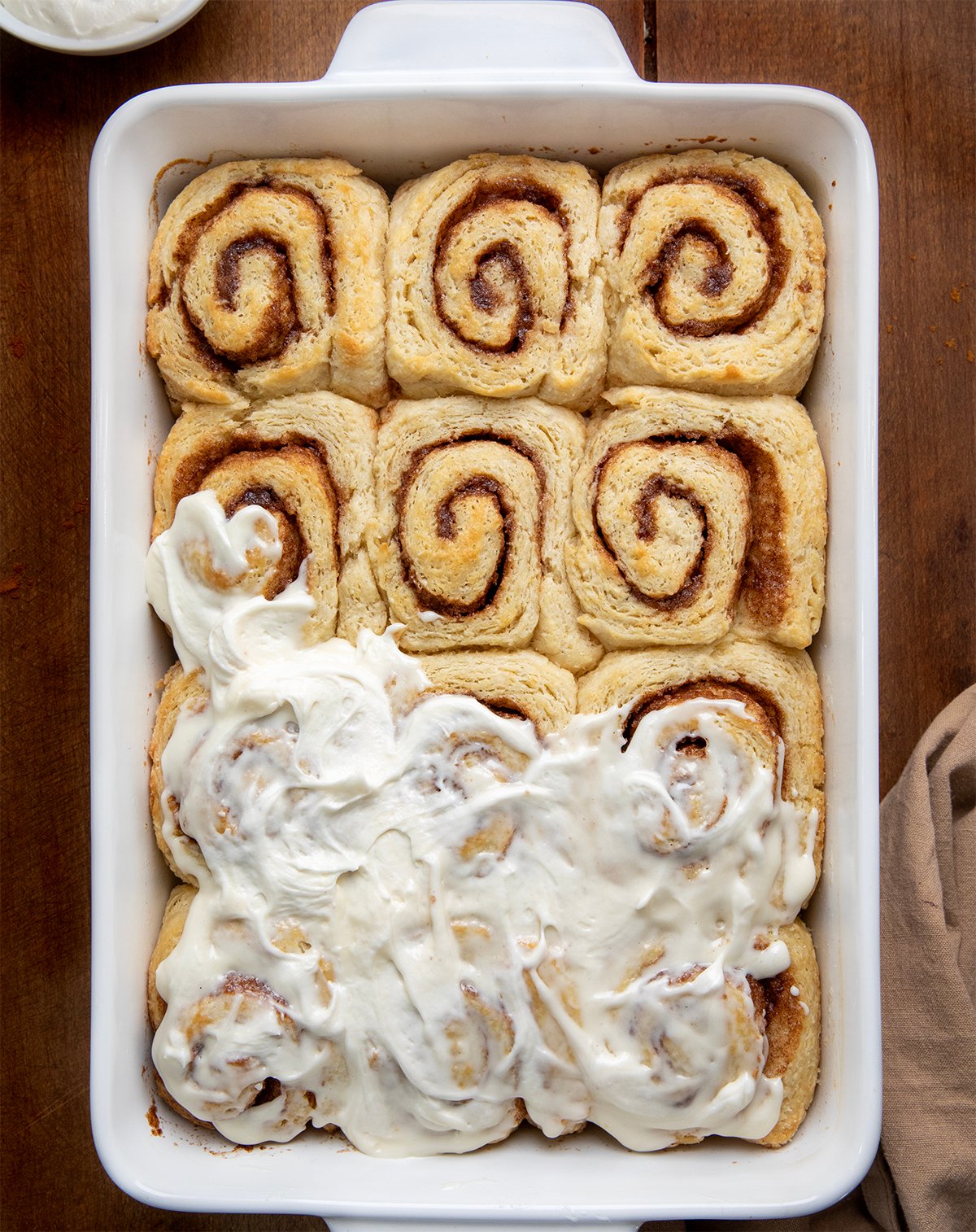 Half frosted Biscuit Cinnamon Rolls on a wooden table from overhead.