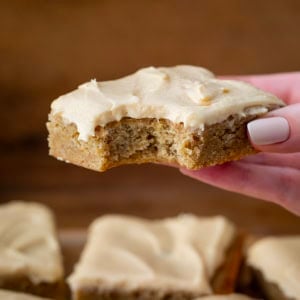 Hand holding a bit into Browned Butter Banana Bars With Salted Caramel Buttercream.