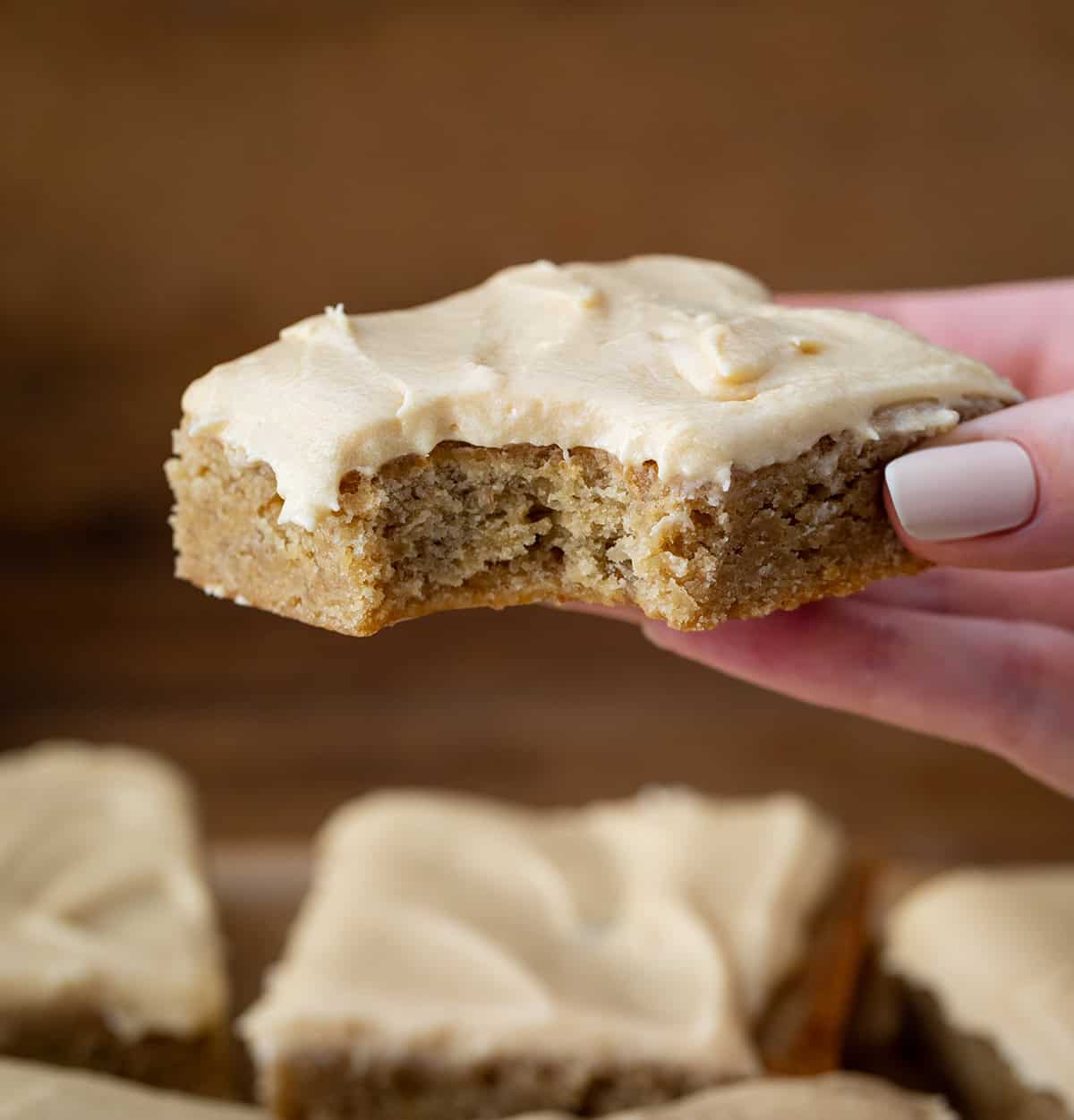 Hand holding a bit into Browned Butter Banana Bars With Salted Caramel Buttercream.