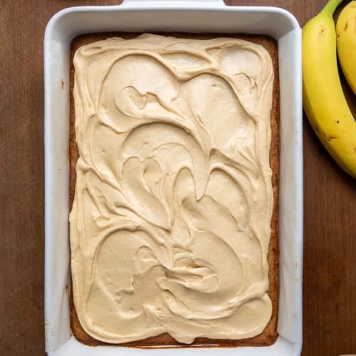 Pan of Browned Butter Banana Bars With Salted Caramel Buttercream on a wooden table next to bananas from overhead.