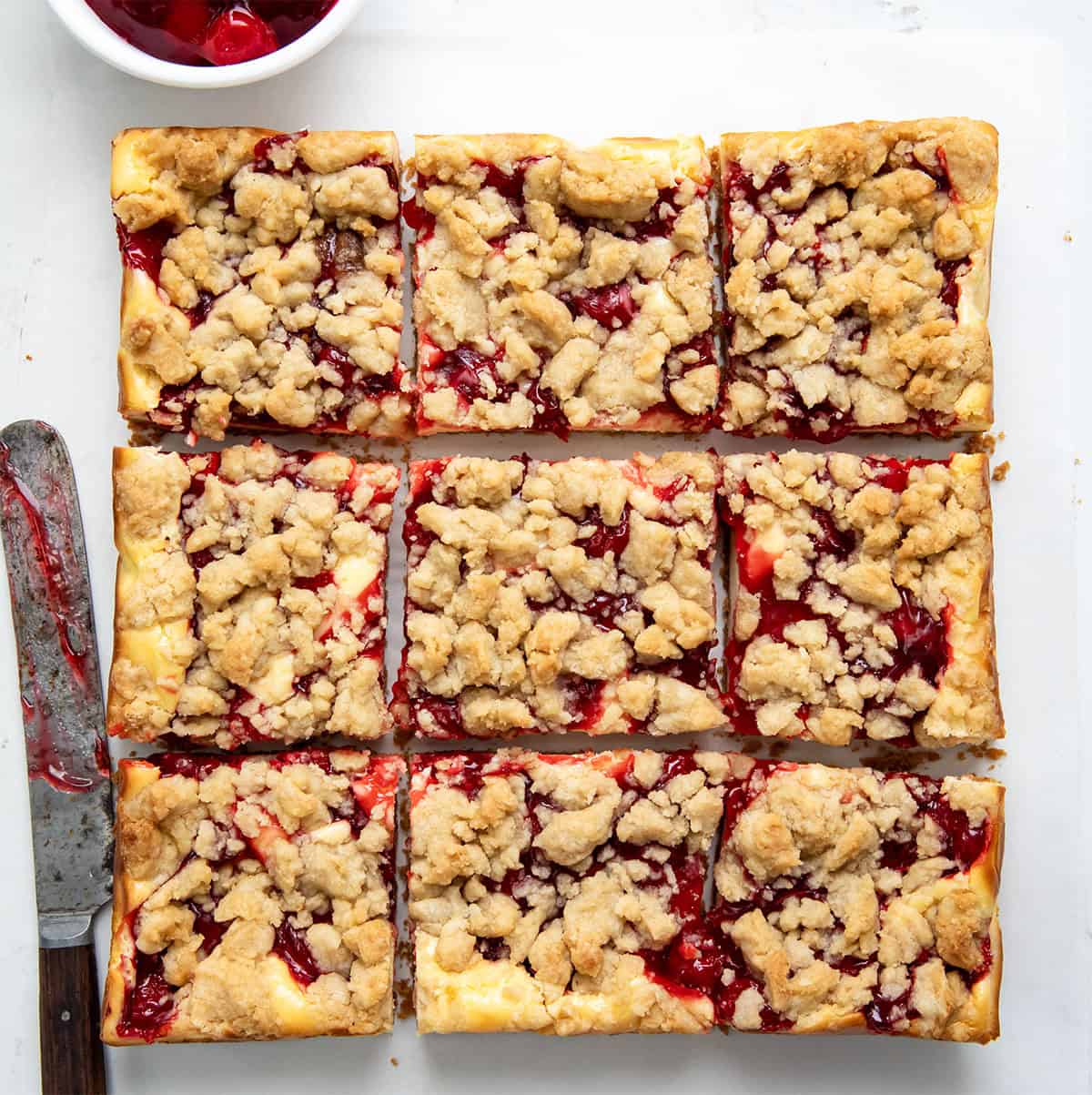 Cherry Almond Cheesecake Bars cut into pieces on a white table from overhead.