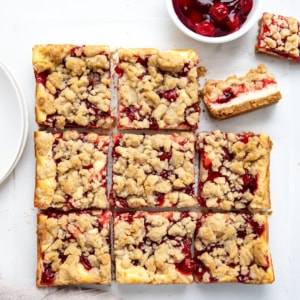 Cut up Cherry Almond Cheesecake Bars with one bar on its side on a white table from overhead.