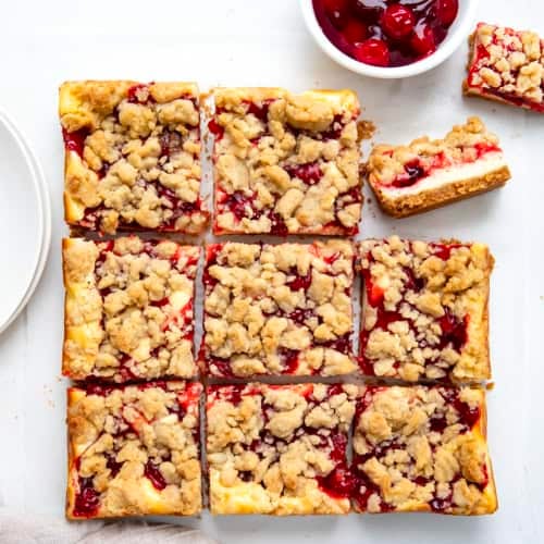 Cut up Cherry Almond Cheesecake Bars with one bar on its side on a white table from overhead.