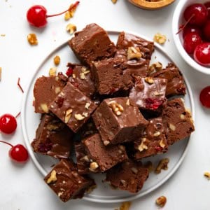 Plate of Cherry Fantasy Fudge cut into pieces with cherries next to it from overhead.